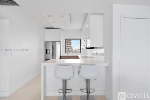 A modern kitchen with white cabinets and a bar area with two stools.