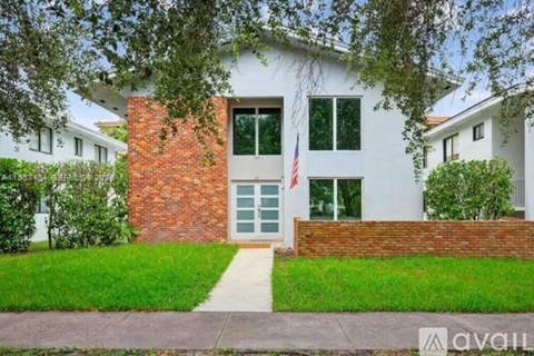 A house with a flag on the front door surrounded by greenery.