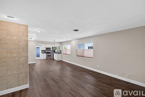 A spacious room with wooden flooring and a stone wall on the left side.