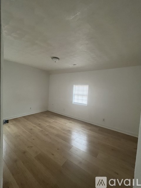 A room with wooden flooring and two windows.
