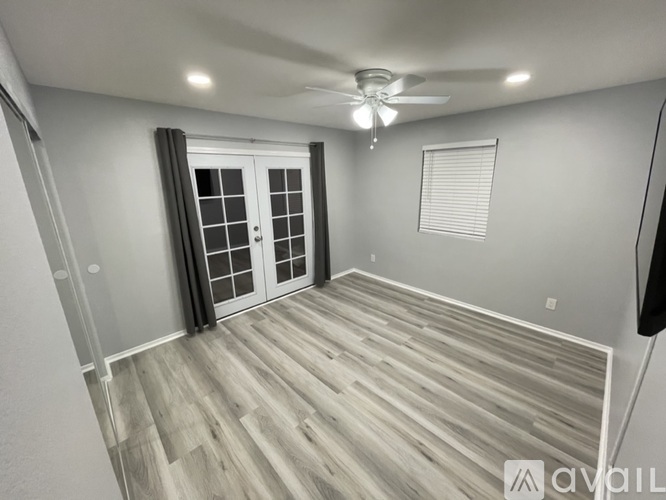 A spacious room with a ceiling fan and lighting, featuring a wooden floor and white walls.