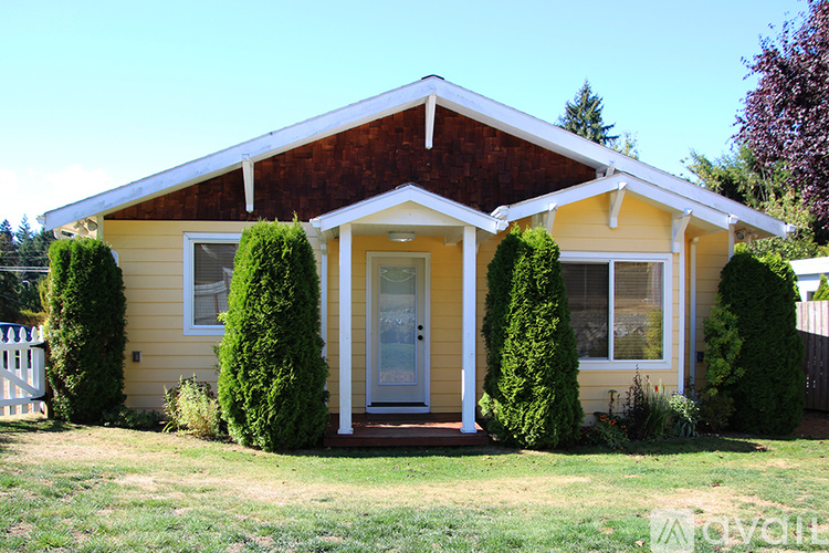 A yellow house with a brown roof and a white fence.
