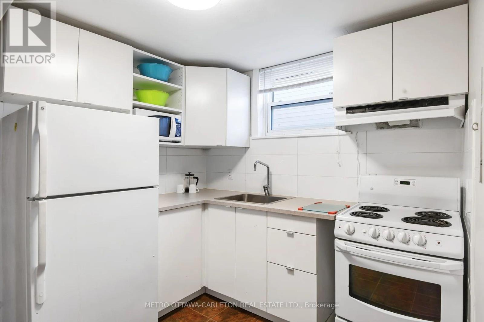 A white kitchen with a stove, sink, and cabinets.