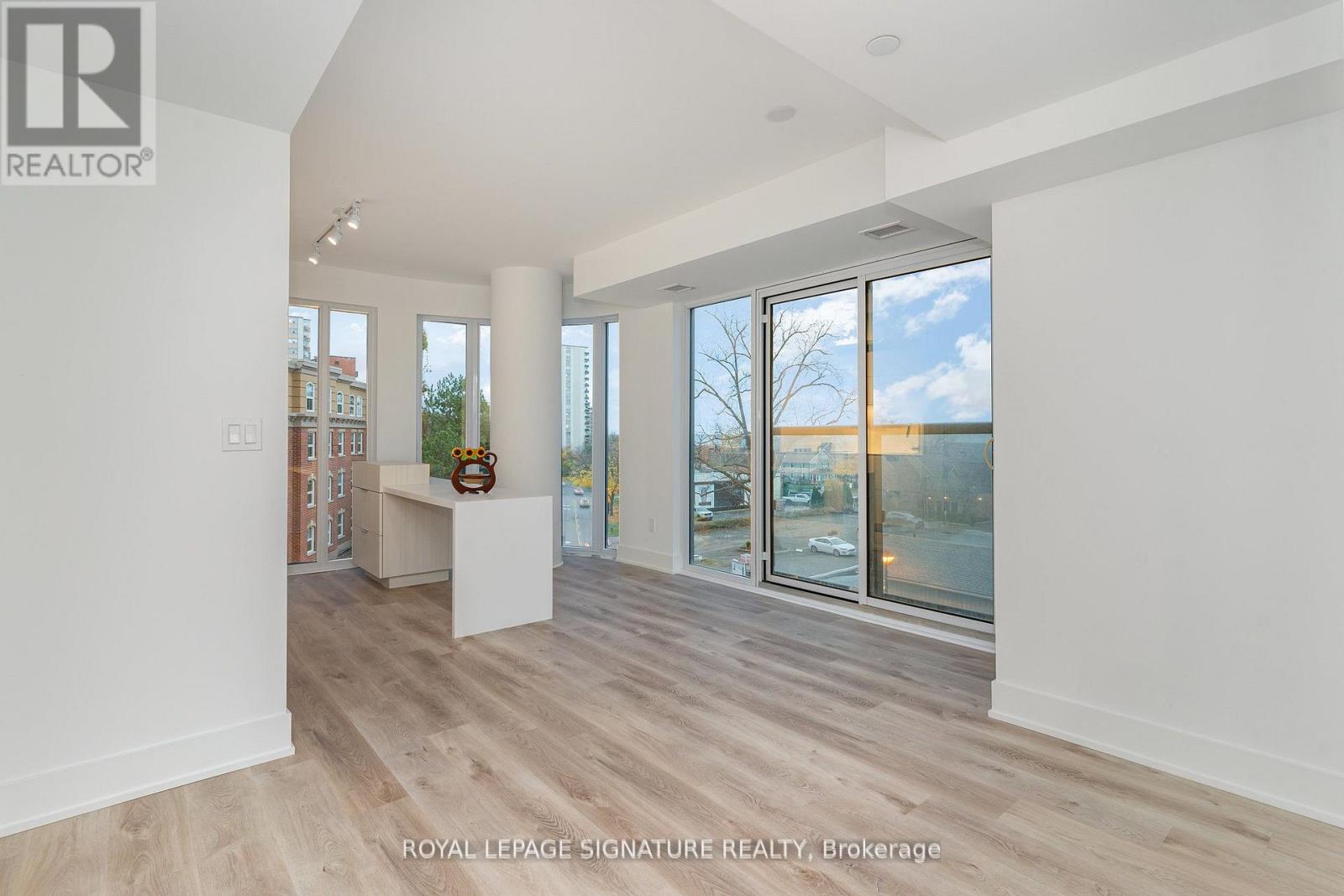 A spacious room with wooden flooring and large windows overlooking a street.