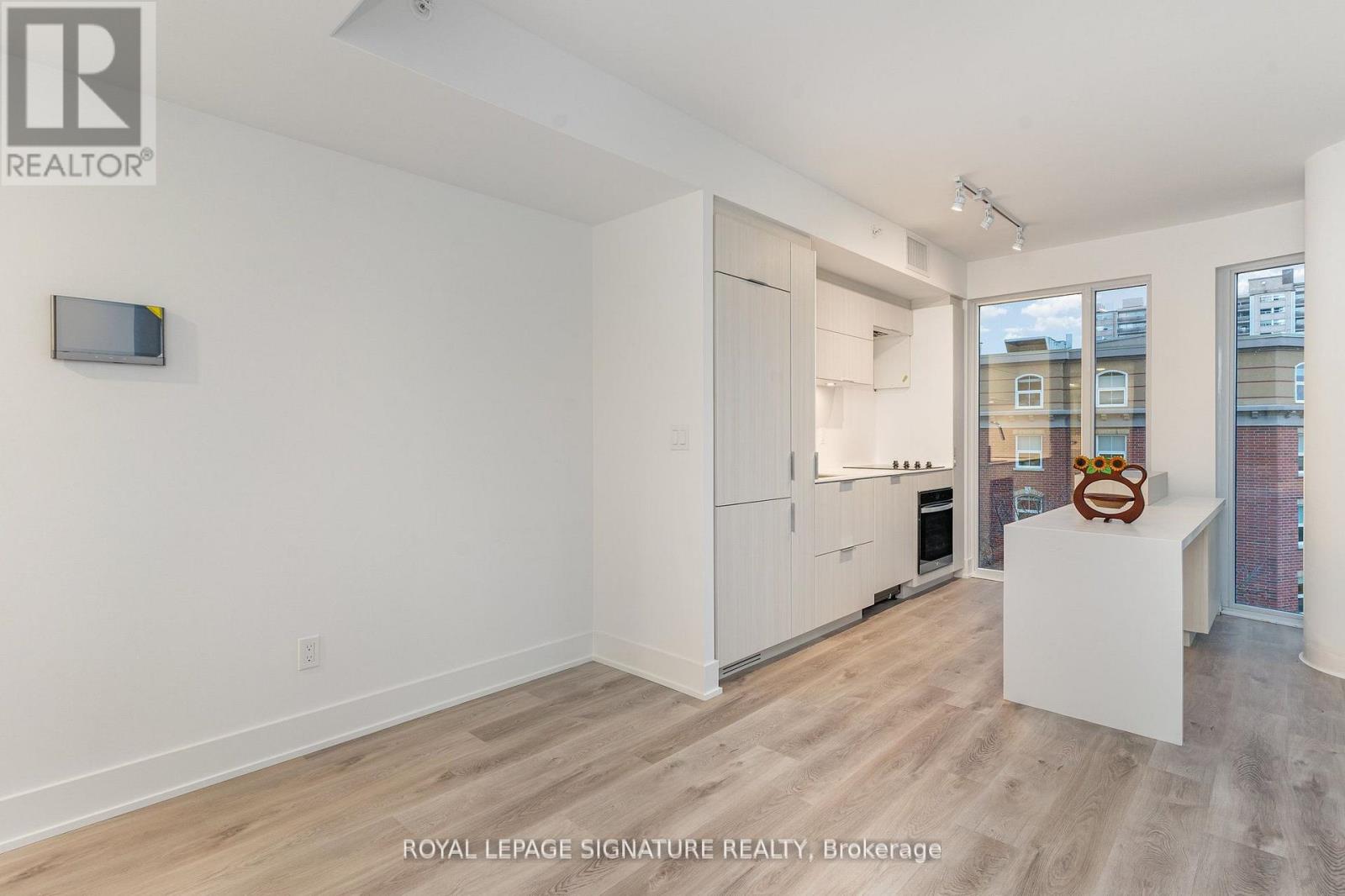 A white room with a wooden floor and a white kitchen area with a fridge, oven and microwave.