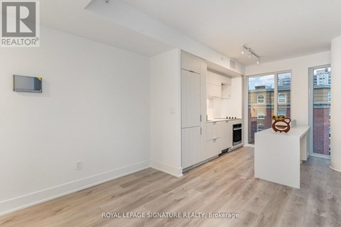 A white room with a wooden floor and a white kitchen area with a fridge, oven and microwave.