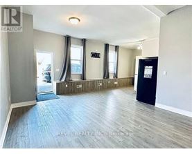 A spacious room with wooden flooring and a black door on the right side.