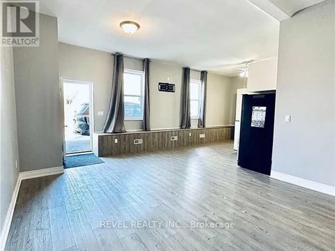 A spacious room with wooden flooring and a black door on the right side.