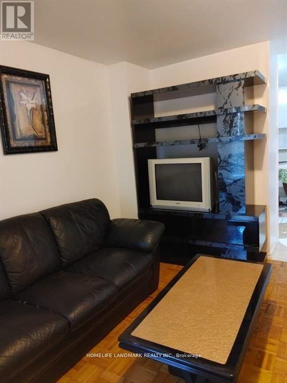 A black leather couch sits in a living room with a television and a picture on the wall.