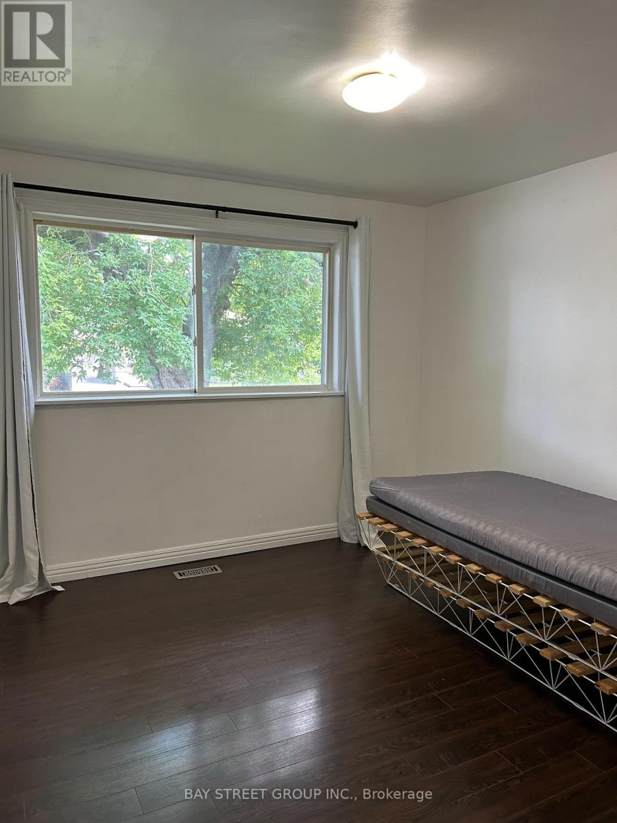 A bedroom with a bed frame and a window with a view of trees.