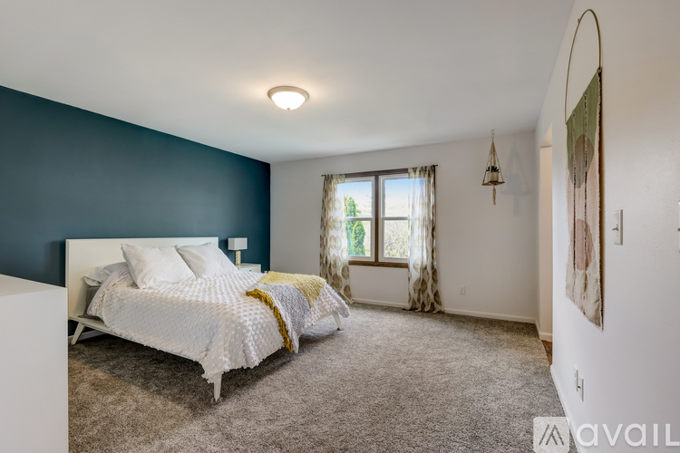 A bedroom with a white bed and a window with curtains.