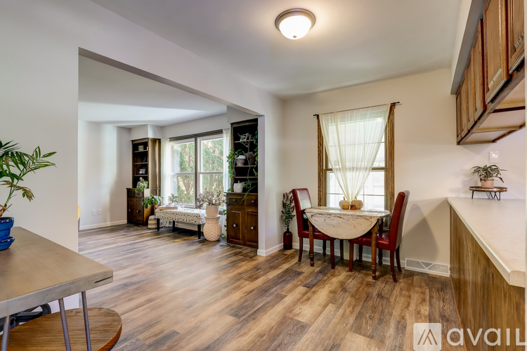 A dining room with a table set for two and a kitchen area with wooden floors.