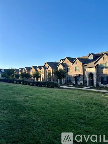 A row of houses with a grassy field in front and a clear blue sky above.