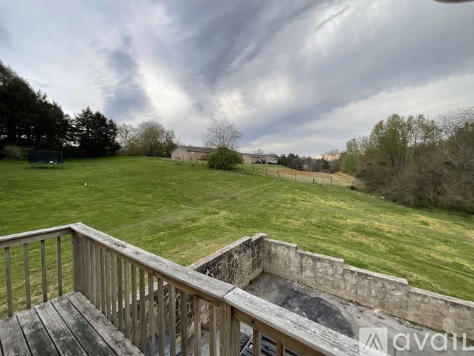 A wooden deck overlooks a grassy field with a cloudy sky above.
