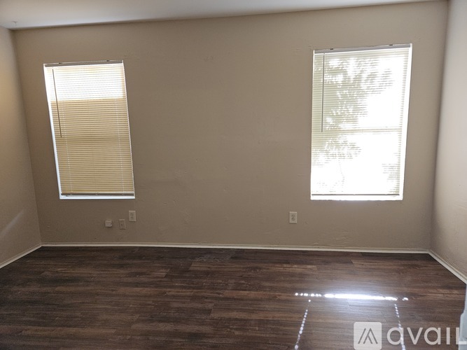 A room with wooden flooring and two windows.