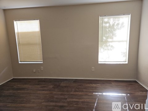 A room with wooden flooring and two windows.