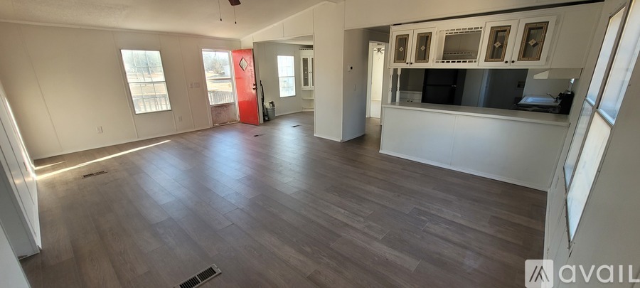 A spacious room with wooden flooring and a kitchen area with white cabinets and appliances.