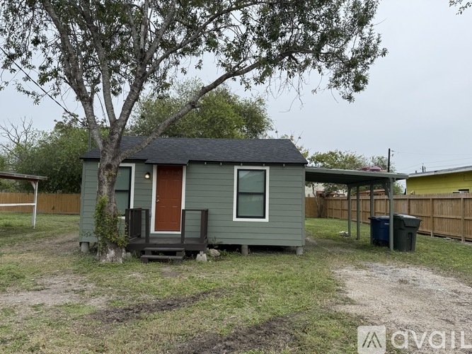 A small house with a red door is surrounded by a fence and a tree.