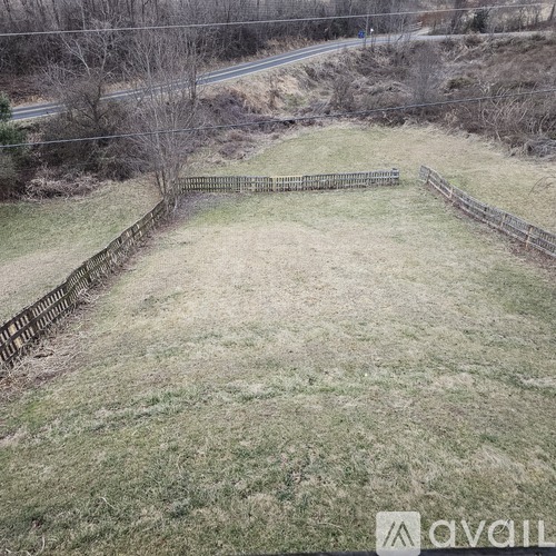 A grassy field with a wooden fence in the foreground and a road in the background.