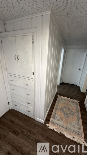 A room with a white wardrobe and a rug on the floor.