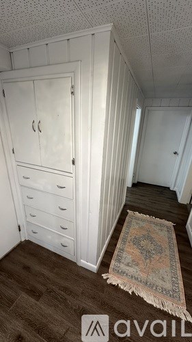 A room with a white wardrobe and a rug on the floor.