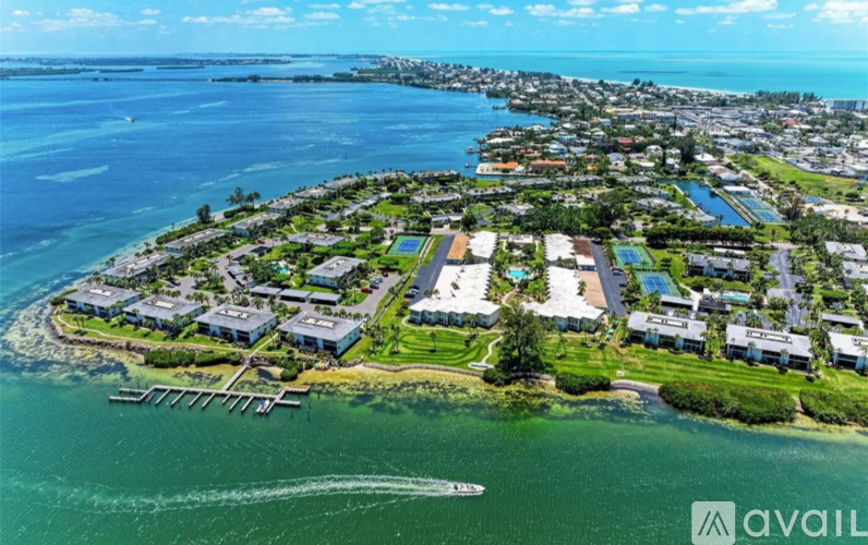 A bird's eye view of a coastal residential area with houses, greenery, and a body of water.