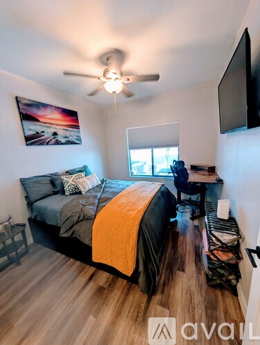 A bedroom with a bed, a ceiling fan, and a painting on the wall.