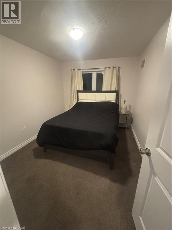 A bedroom with a bed, carpeted floor, and a window with curtains.