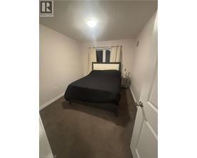 A bedroom with a bed, carpeted floor, and a window with curtains.