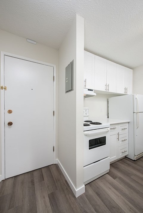 A white door with a brass handle is in a kitchen with white appliances.