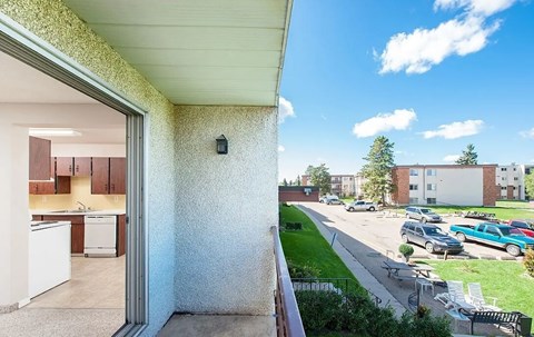 A view from a window of a building with a balcony overlooking a parking lot.