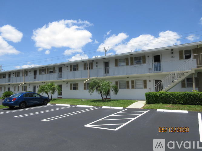 A blue car is parked in a parking lot in front of a white building.