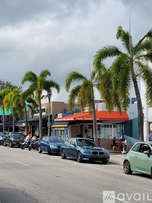 Cars parked on a street with palm trees and a Philly Chicken restaurant in the background.