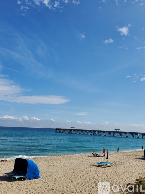 A beach scene with a pier in the distance and people relaxing on the sand.