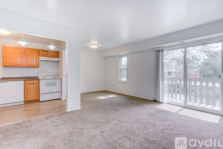 A well-lit, empty living room with a kitchen area and sliding glass doors leading to a balcony.