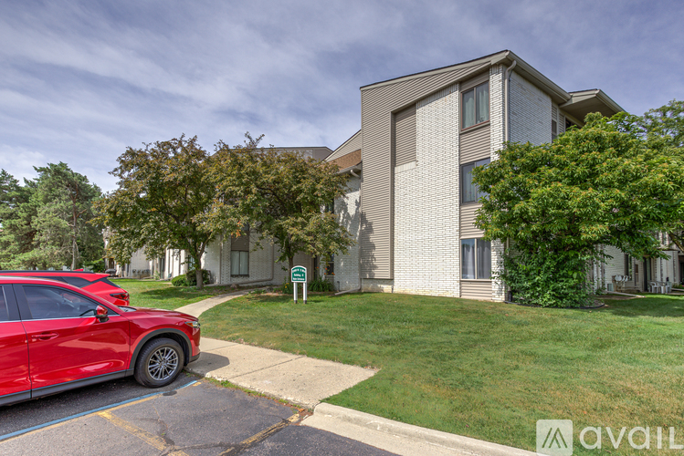 A red car is parked in a parking lot in front of a building.