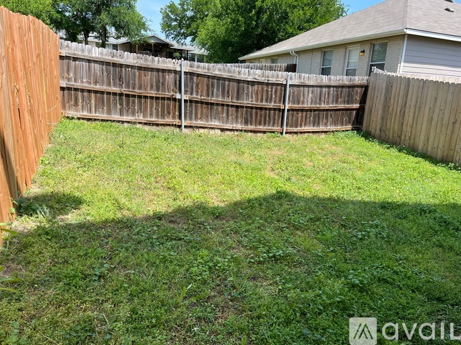 A backyard with a wooden fence and a house in the background.