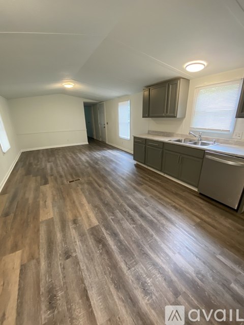 A spacious room with wooden flooring and a kitchen area with a sink and cabinets.