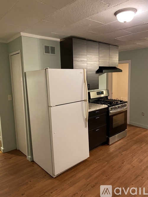 A white refrigerator in a kitchen with wooden floors and a stove top oven.
