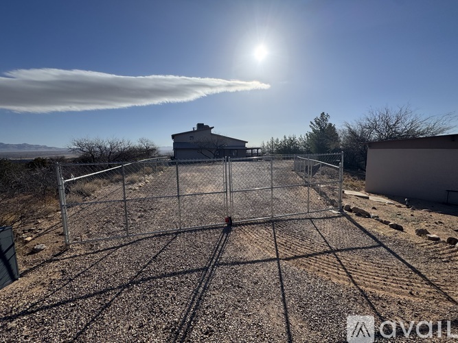 A sunny day with a large cloud formation over a fenced area with a building in the background.