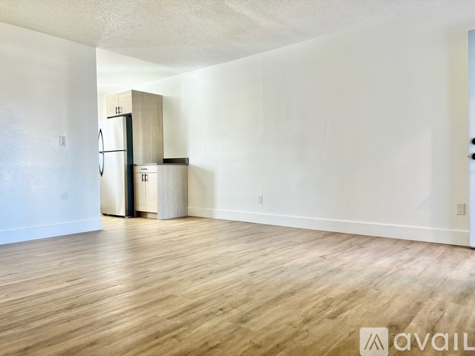 A spacious room with wooden flooring and a refrigerator in the corner.
