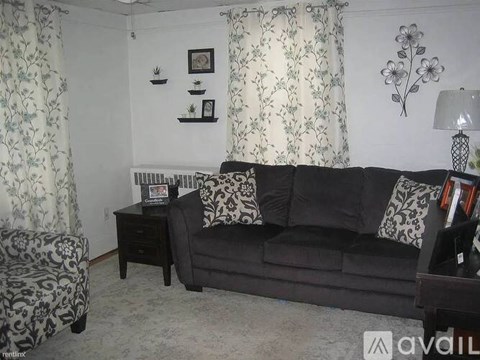 A living room with a black couch, a chair, and a small table with a lamp.