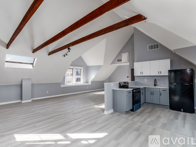 A spacious, well-lit attic room with wooden beams and a kitchen area.