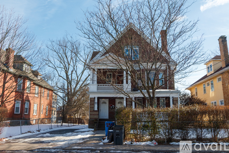 A house with a red brick chimney is in front of a tree and other houses.