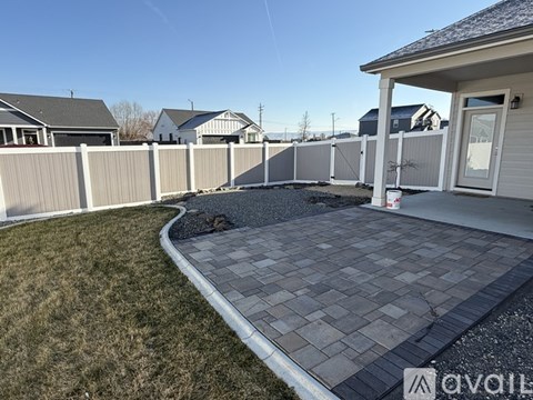 A backyard with a paved walkway and a white fence.