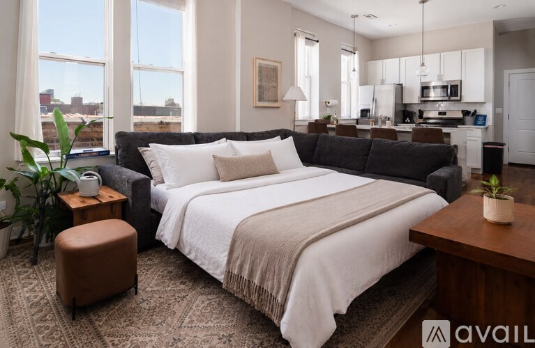 A bedroom with a large bed and a kitchen area in the background.