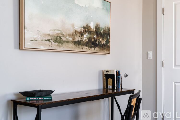 A painting hangs on a wall above a table with a bowl, books, and a small box on it.