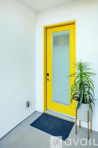 A yellow door with a glass panel is flanked by two potted plants.