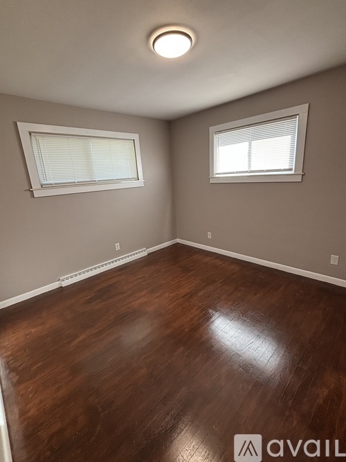 A room with wooden flooring and a window with white curtains.