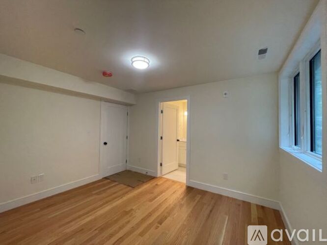 A room with wooden flooring and white walls, with a doorway leading to another room.
